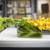Cymbidium orchids, bells &amp; trick in a leaf wrapped glass rectangle container.