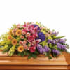 A full and lush multicolored casket spray of roses, lilies, snapdragons, and