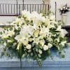 Beautiful and elegant white casket arrangement featuring lilies, orchids, roses, carnations, and