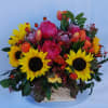 An arrangement of bright sunflowers, tulips, spray roses, proteas, and peonies accented