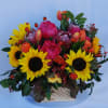 An arrangement of bright sunflowers, tulips, spray roses, proteas, and peonies accented