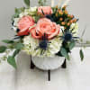 Modern white ceramic with wood stand is filled with hydrangeas, roses, thistle