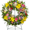 A bright standing wreath of greenery and fresh flowers in yellow, pink