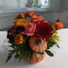 Orange pumpkin container with bright seasonal flowers.