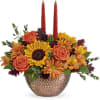 This stunning centerpiece features medium yellow sunflowers, orange carnations, bronze daisy spray