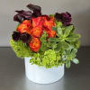 Roses and other flowers are arranged together in a white ceramic vase