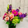 A low and compact arrangement of roses, hydrangeas, and lilies in purple