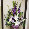Seasonal flowers in shades of purple and white in a mache container.