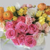 This arrangement includes pink roses, yellow spray roses, orange ranunculus and white