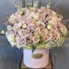 Soft colored roses, larkspur arranged in a tall hat box.  This