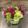 A modern style arrangement of greens and purples, including roses, tulips, orchids