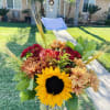 An arrangement of sunflowers, roses, and daisies, accented with barley, solidago, and