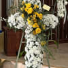A white cross on a stand with a spray of yellow roses.