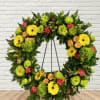 A wreath display on an easel mixed with radiantly bright flowers. 
