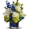 Stunning blue, white and green flowers designed in a blue cube vase