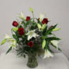 A tall vased arrangement of red roses and white lilies in a