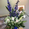 Blue delphiniums, white lilies, roses and alstroemerias,in a blue container as available.
