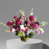 Pinks and purples surrounded by seasonal foliage and flowers in a glass