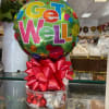 A Get Well balloon with a pink bow and a small rose arrangement beside it.