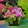 An arrangement in a clear vase with roses, orchids, fillers, and greenery