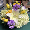 White, purple, yellow flowers in a short vase. 