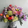 A beautiful and vibrant floral arrangement featuring dahlias, anemones, roses, lilies, and