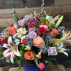 The &quot;Whispering Wilds&quot; bouquet combines multicolored roses, lush greenery, elegant lilies, fragrant