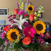 An arrangement of sunflowers mixed in with bright colored flowers arranged in