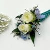 A boutonniere  featuring white spray roses, blue belladonna, turquoise ribbon and