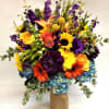 This bright arrangement comes complete with aziatic lilies, delphinium, roses, gerbera daisies