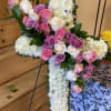CROSS WITH PURPLE ROSES IN THE CENTER WITH GREENARY AND WHITE CUSHION.
