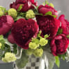 This arrangement includes rich burgundy peonies with green accents in a shiny