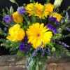 This sunny bouquet in yellows and purples, featuring gerberas and roses will