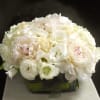 White/pink-blushed peonies, white lisianthus, cream roses, campanula in a clear rectangle vase