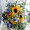 Traditionally rounded bridal bouquet featuring sunflowers and seasonal blue blooms. Ivory ribbon