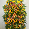 This sympathy spray includes sunflowers, roses, tulips, calla lilies, and seasonal greens.