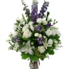 Mostly white vase arrangement with exceptional purple or blue floral accents. Designed