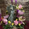A beautiful arrangement of Spring colored flowers surrounding a resin angel arranged