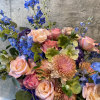 An airy arrangement crafted with various roses, delphinium, hydrangeas, mums, hellebores, and