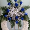 Open wreath with white carnations, white lilies, and blue roses.