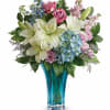This arrangement features blue hydrangea, lavender roses, white asiatic lilies, light blue