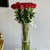 Two Dozen long stemmed red roses stand tall in a glass cylinder