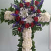 Cross with white hydrangeas, red roses, white lilies, and purple larkspurs.