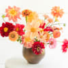 this asymmetrical arrangement features vibrant orange and red blooms, artfully crafted to