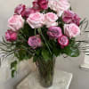 A tall clear glass vase holds an arrangement of two dozen roses