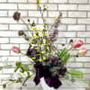 A white basket arranged with artificial tulips, delphinium, ranunculus, hydrangea, along with