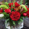 Red roses arranged in a clear glass cube with holiday greens and
