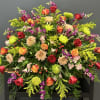 Bright and colorful casket spray. Featuring red roses, high magic roses, cremons