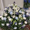 A elegant tribute with blue/white carnations, white roses, white lilies, blue delphinium