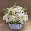 All white flowers mounded all around in a white wicker basket.